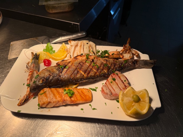 Gegrillter Fisch mit Garnelen, Lachs, Zitronenscheiben und Petersilie auf weißem Teller