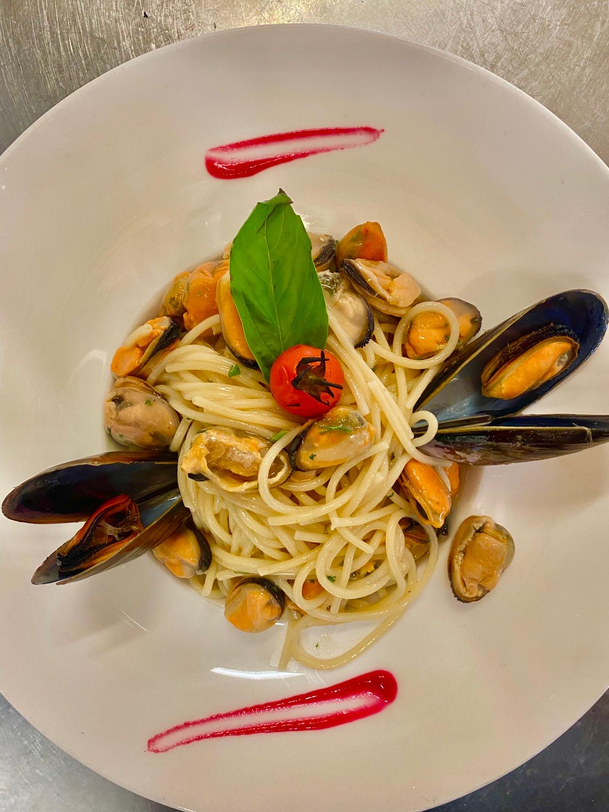 Ein Teller mit Spaghetti und Muscheln, garniert mit Basilikum und roter Sauce